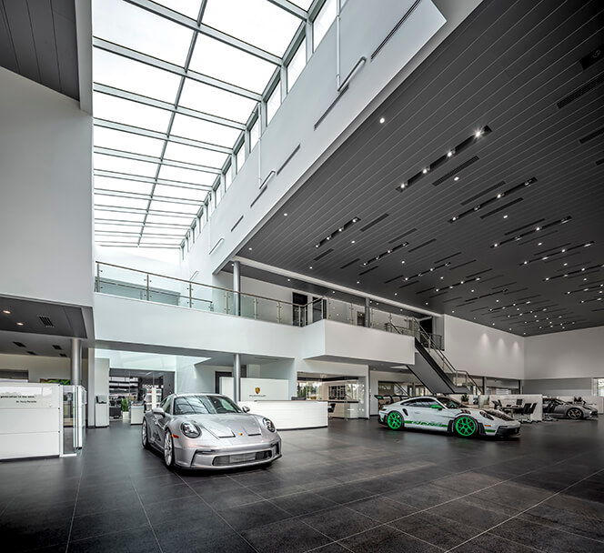 Inside a Porsche dealership with one grey Porsche and one white Porsche with green sports wheels.